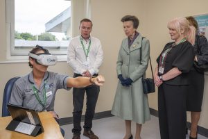 Her Royal Highness The Princess Royal in a room at RABIU where one person is wearing a VR headset and has their arm outstretched.